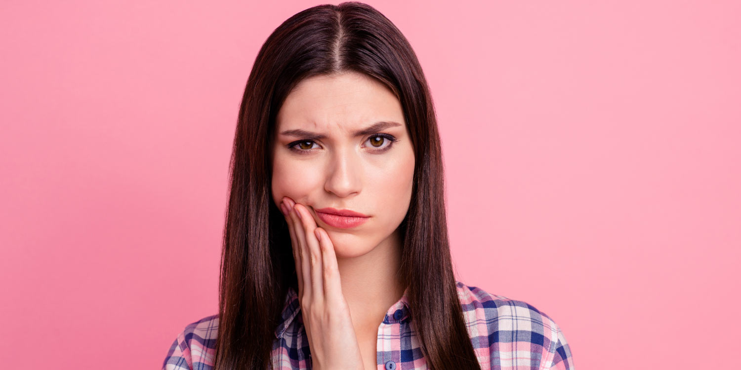 Brunette woman in a plaid shirt cringes and frowns because of her braces pain