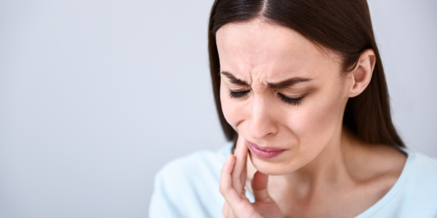 Brunette woman touches her cheek due to braces pain