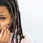 Young girl with braces cringes and touches her cheek because of an orthodontic emergency