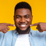 Dark-haired man points to his straight teeth after orthodontic treatment in Weatherford, TX