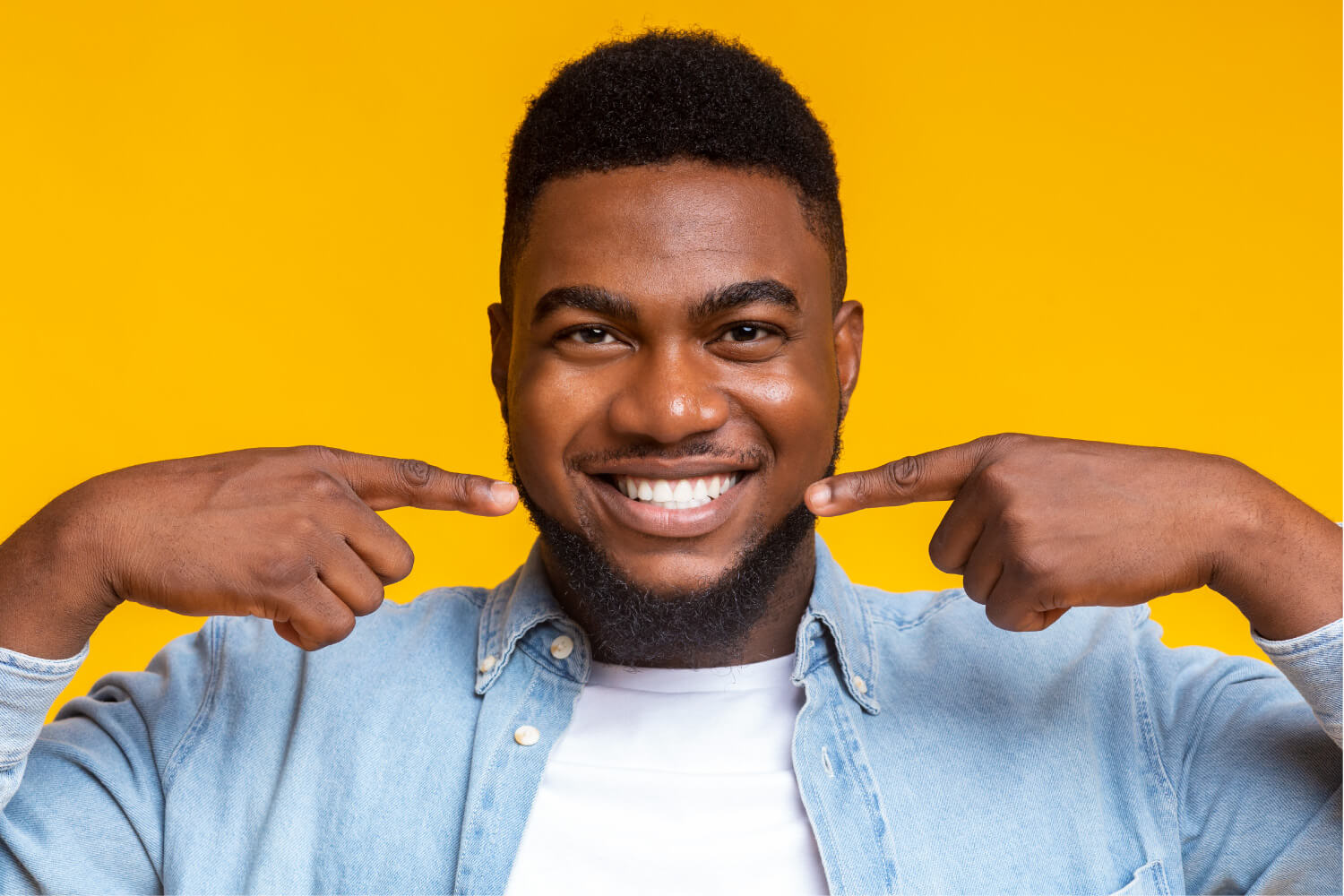 Dark-haired man points to his straight teeth after orthodontic treatment in Weatherford, TX