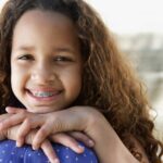 Brunette girl with early orthodontics smiles with her chin on her knees