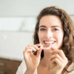 Brunette smiling woman holding a clear aligner.