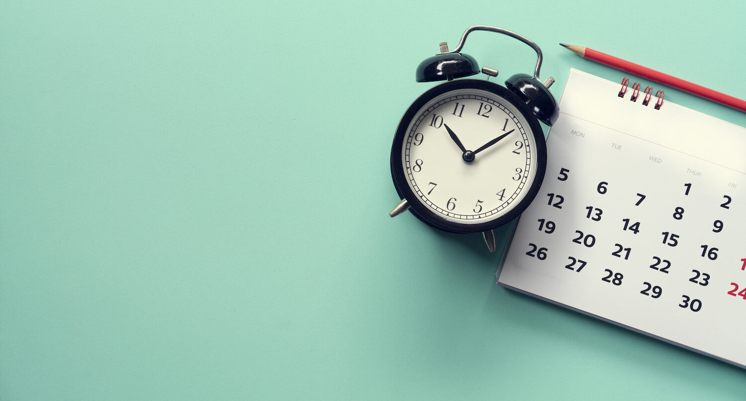 Aerial view of an alarm clock next to a calendar on an aqua green background